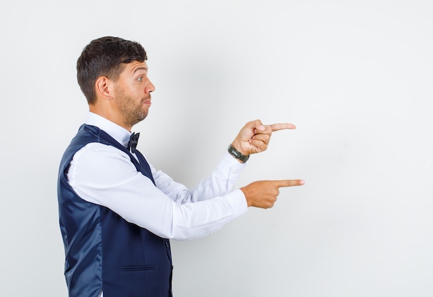 Waiter in shirt, vest pointing fingers to side and looking motivated .