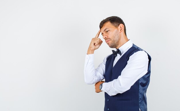 Waiter in shirt, vest thinking with finger on temples and looking sad , front view.