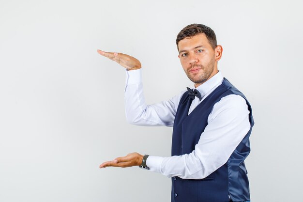 Waiter showing large size sign in shirt, vest, bow tie , front view.