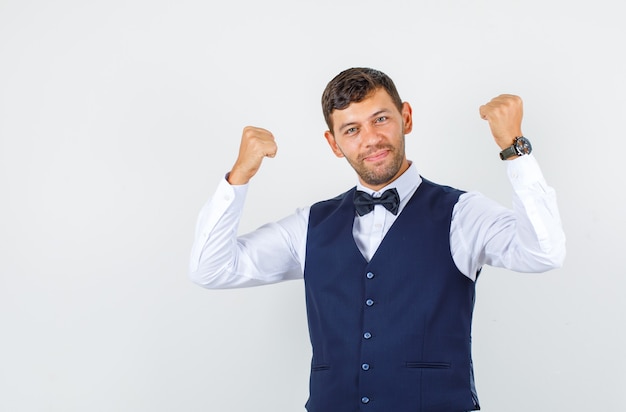 Foto gratuita cameriere che mostra il gesto del vincitore e sorridente in camicia, gilet e che sembra felice. vista frontale.