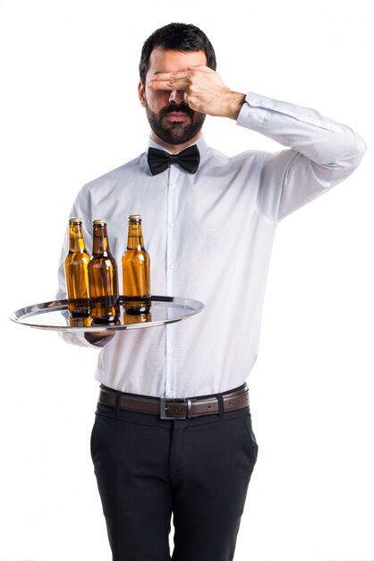 Waiter with beer bottles on the tray covering his eyes