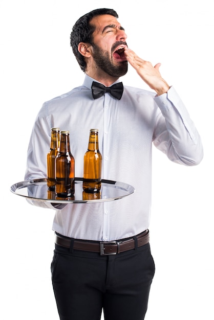 Waiter with beer bottles on the tray yawning