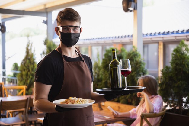 waiter works in a restaurant in a medical mask, gloves during coronavirus pandemic