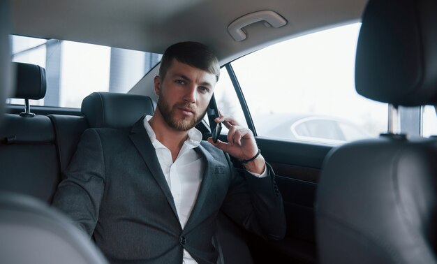答えを待っています。車の後ろに座っているときに公式の摩耗のビジネスマンが電話をしています