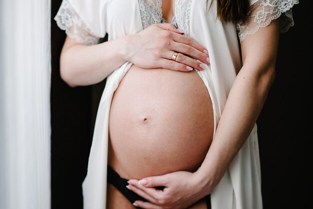 Waiting baby. pregnant woman standing and hands embraces a round belly, stomach. close-up. nine months. baby shower. motherhood concept. front view.