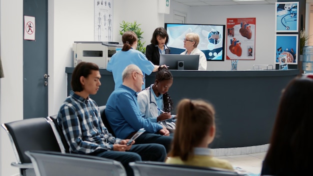 Waiting room in hospital lobby with reception counter desk, diverse people waiting to attend checkup visit appointment. Health care examination in emergency area at medical clinic.