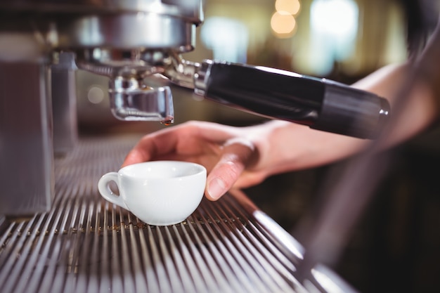 Waitress making cup of coffee at counter in kitchen