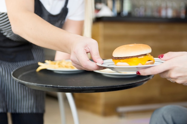 Waitress serving burger to female customer in the restaurant