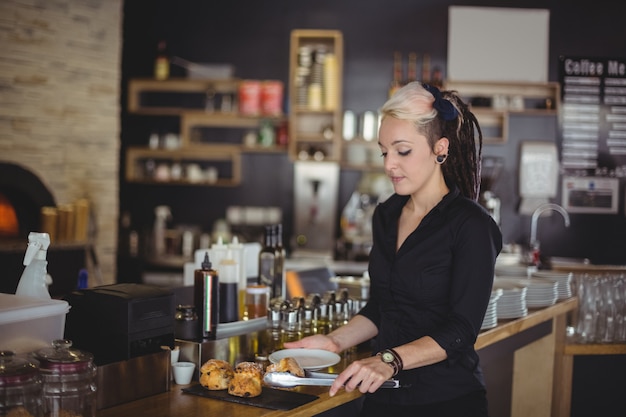Waitress serving muffin in a plate at counter