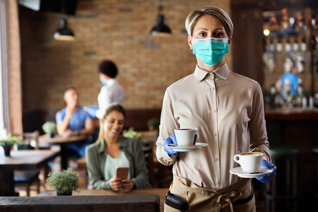 Waitress with protective face mask and gloves serving coffee in a cafe