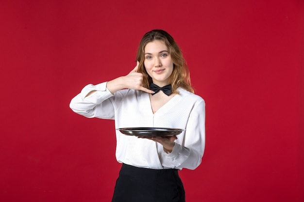 Free photo waitress woman butterfly on the neck and holding tray making call me gesture on red background