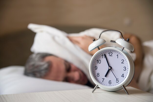 Waked Up Man lying in bed turning off an alarm clock in the morn