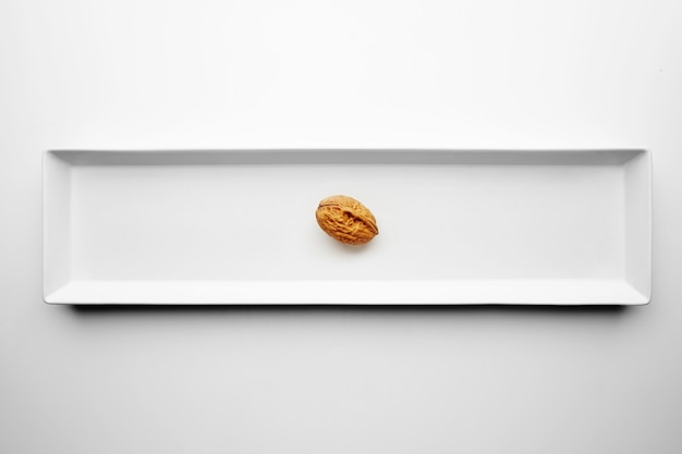 Walnut alone isolated in center of rectangular ceramic plate on white table