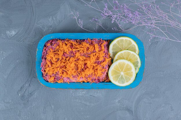 Walnut and beet salad topped with carrot and garnished with lemon slices on marble background.