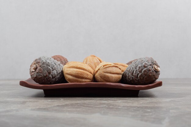 Walnut shaped cookies and pinecones on dark plate.