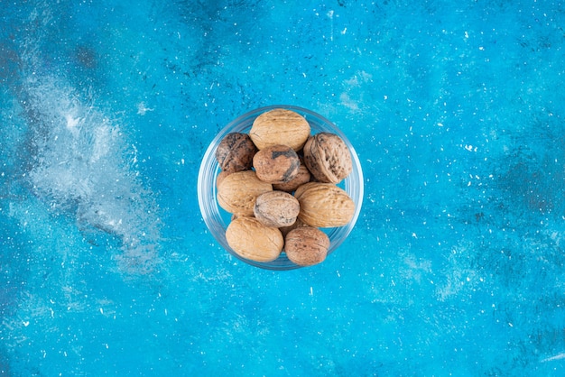 Бесплатное фото Грецкие орехи в скорлупе в стеклянной миске на синей поверхности