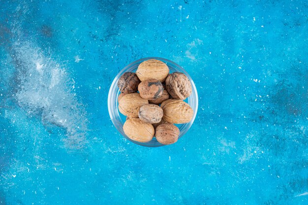 Walnuts in shell in a glass bowl on the blue surface