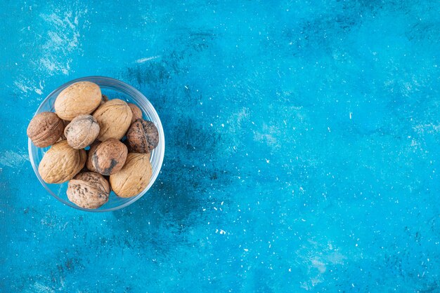 Walnuts in shell in a glass bowl , on the blue table. 