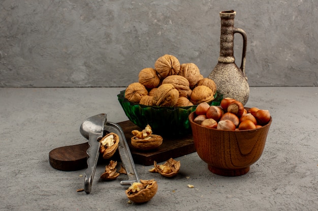 Грецкие орехи целые вкусные фундуки внутри коричневого горшка и зеленой тарелке на сером столе