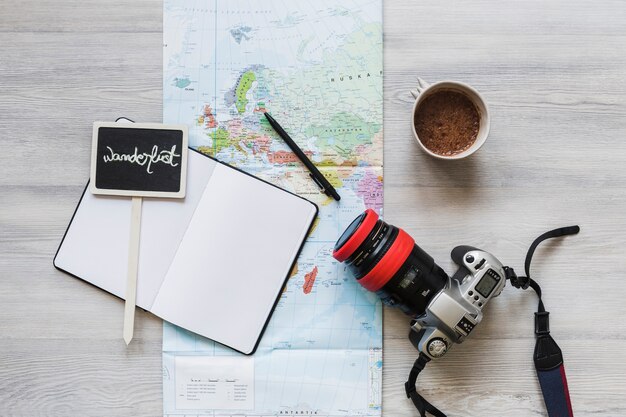 Wanderlust placard over the notebook with map, coffee and camera on desk