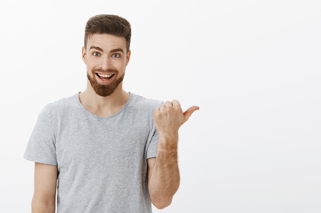 Wanna see something curious. Portrait of enthusiastic happy handsome caucasian guy with beard and moustache pointing right and smiling joyfully passionately talking about awesome copy space