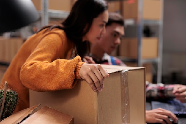 Free photo warehouse employees holding package and creating invoice on laptop