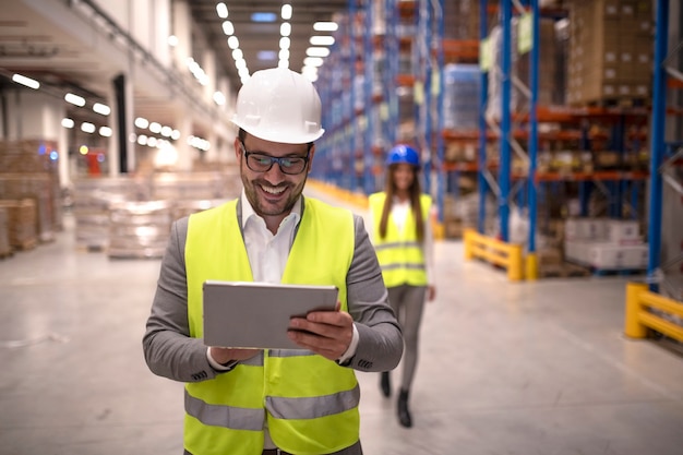 Warehouse manager reading report on tablet about successful delivery and distribution in warehouse logistics center