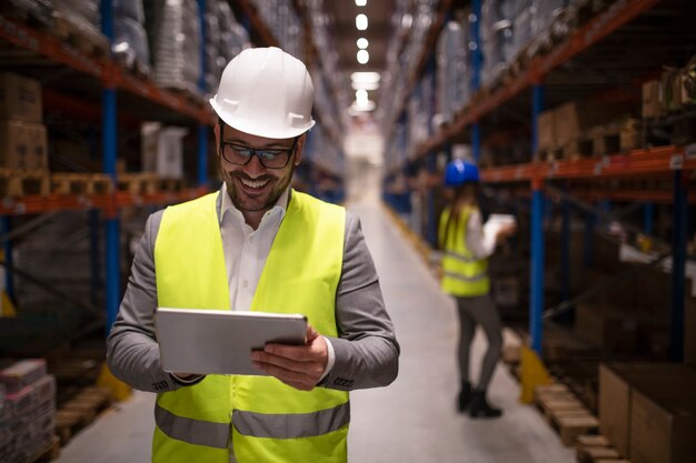Warehouse supervisor reading report on tablet about successful delivery and distribution in warehouse logistics center