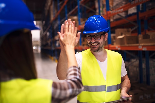 Warehouse worker giving high five to his friend colleague