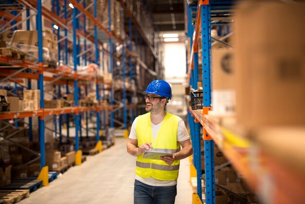 Работник склада держит планшет и проверяет запасы в большом распределительном складском центре