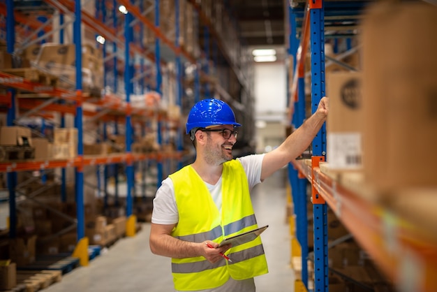 Warehouse worker looking at shelves with packages and checking inventory of large warehouse storage distribution area