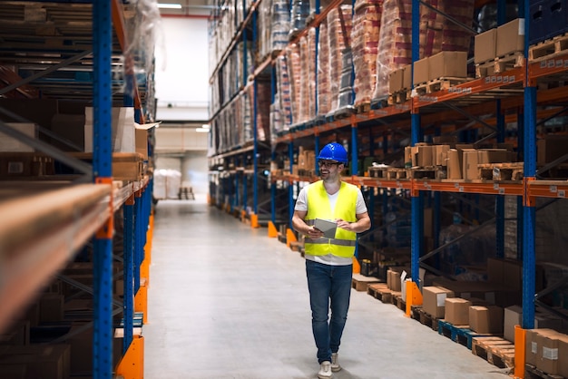 Warehouse worker looking at shelves with packages and walking through large warehouse storage distribution area