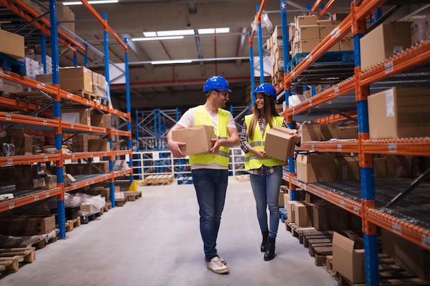 Warehouse workers carrying boxes in storage area putting them on shelves