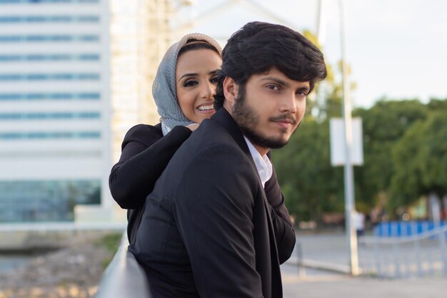 Warm Arabic couple spending time together. Woman with covered head and bright make-up and man in suit sitting on bench. Love, affection concept