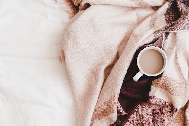 Warm drink in striped plaid on bedsheet