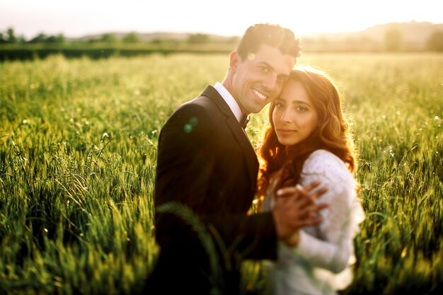 Warm evening sun illuminates wedding couple kissing on the field