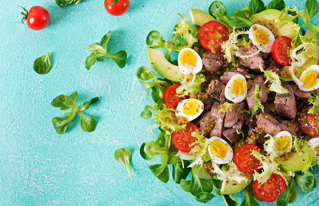 Warm salad from chicken liver, avocado, tomato and quail eggs. Healthy dinner. Dietary menu. Flat lay. Top view