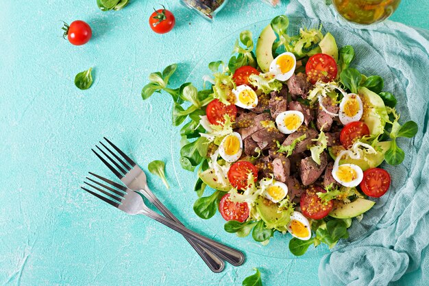 Warm salad from chicken liver, avocado, tomato and quail eggs. Healthy dinner. Dietary menu. Flat lay. Top view