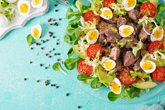 Warm salad from chicken liver, avocado, tomato and quail eggs. Healthy dinner. Dietary menu. Flat lay. Top view