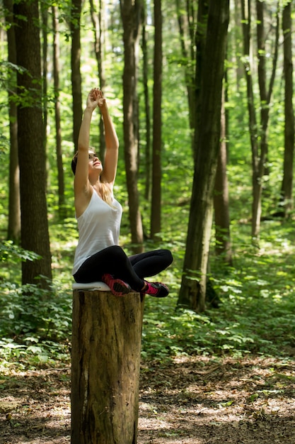 Riscaldamento. bella ragazza sportiva nel bosco su un ceppo di yoga, sport