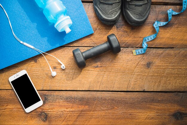 Water bottle; sport shoes; earphone; cellphone; dumbbells and measuring tape on wooden background