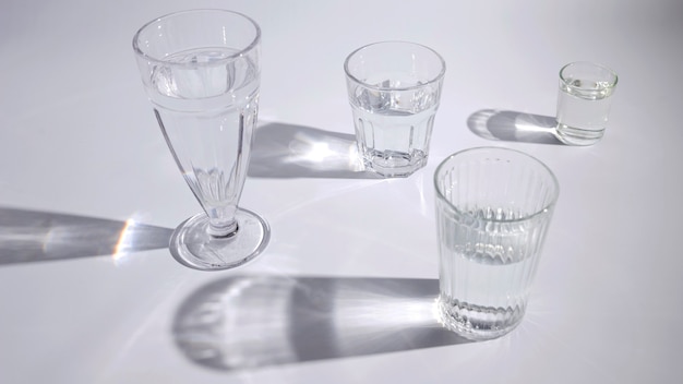 Water in the different type of glasses with shadow on white backdrop