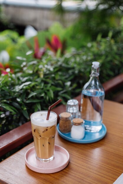 Water in glass bottle iced latte on a pink stand salt and paper On wooden table