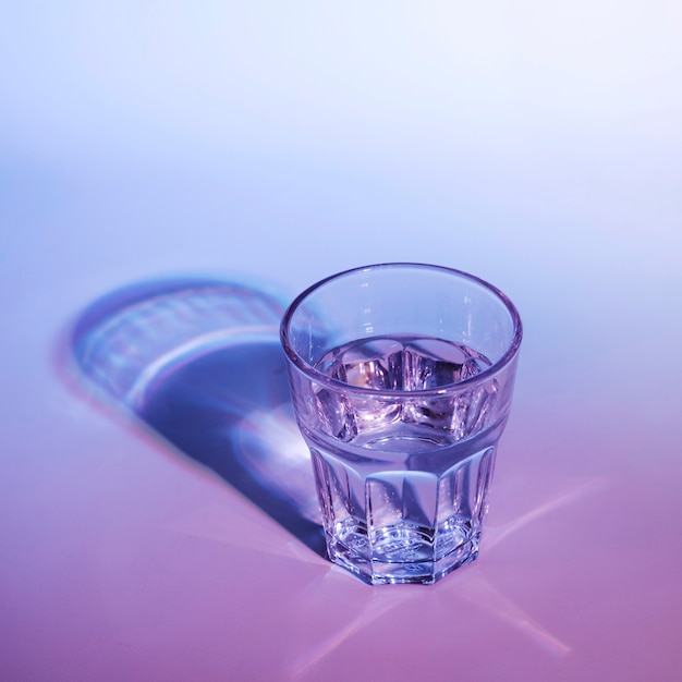 Water glass with dark shadow on blue and pink background