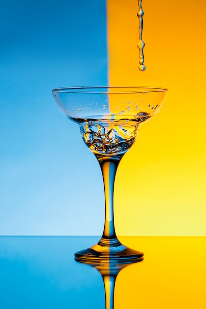 Water pouring in glass over blue and yellow wall