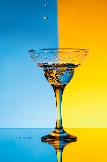 Water pouring in glass over blue and yellow wall