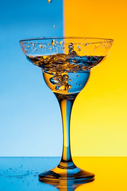 Free photo water pouring in glass over blue and yellow wall