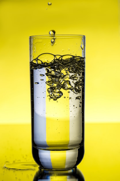 Water pouring in glass over yellow wall