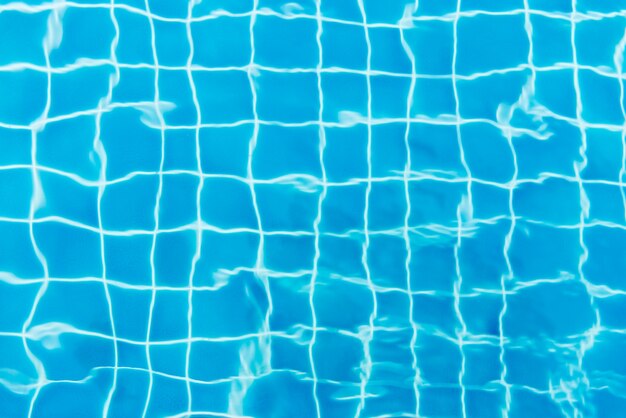 Water ripples on blue tiled swimming pool background. View from above.