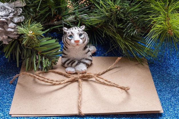 The water tiger is the symbol of the chinese new year 2022. a figurine of a lying tiger holding a craft envelope on a blue shiny background like on water with branches of an artificial spruce.